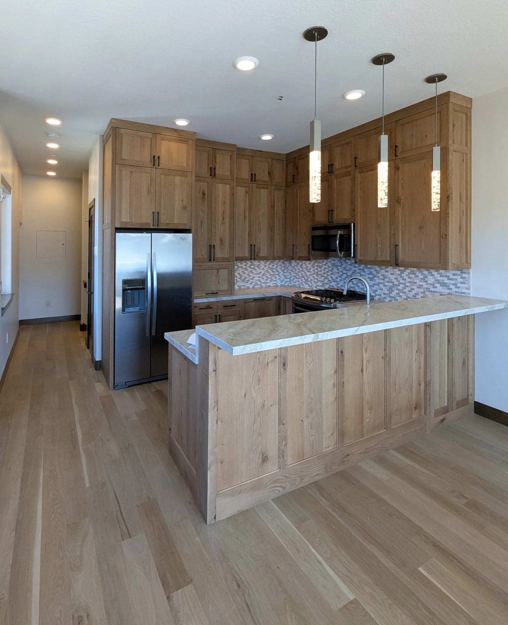 Kitchen with white oak cabinetry, a stone peninsula and pendant lighting