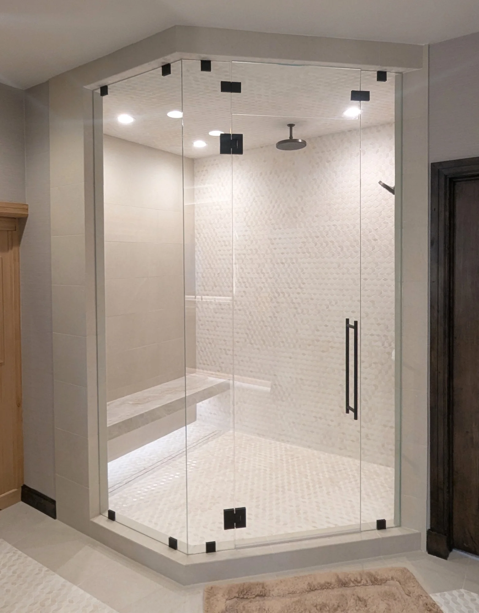 Frameless glass steam shower with marble mosaic tile and a floating bench