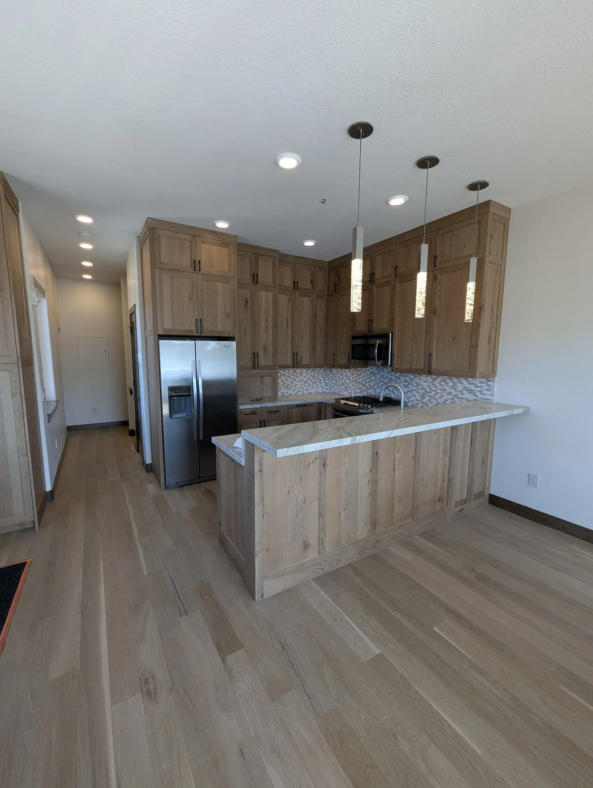 Kitchen with white oak cabinetry to the ceiling, a stone-topped peninsula and three pendant lights